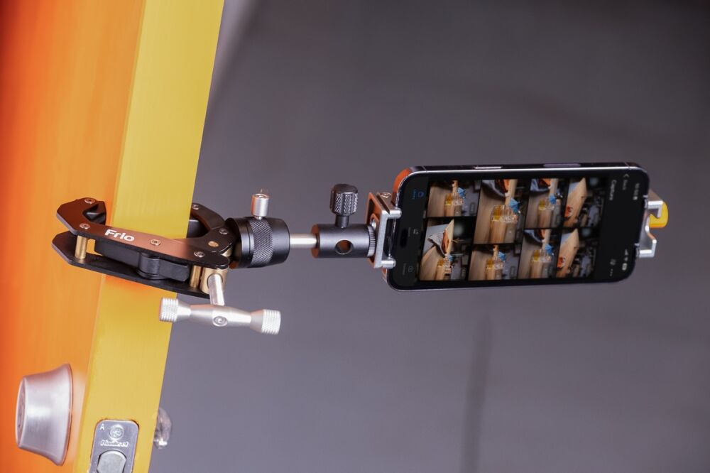 Smartphone mounted on a clamp rig attached to an orange stand, screen displaying a grid of photos
