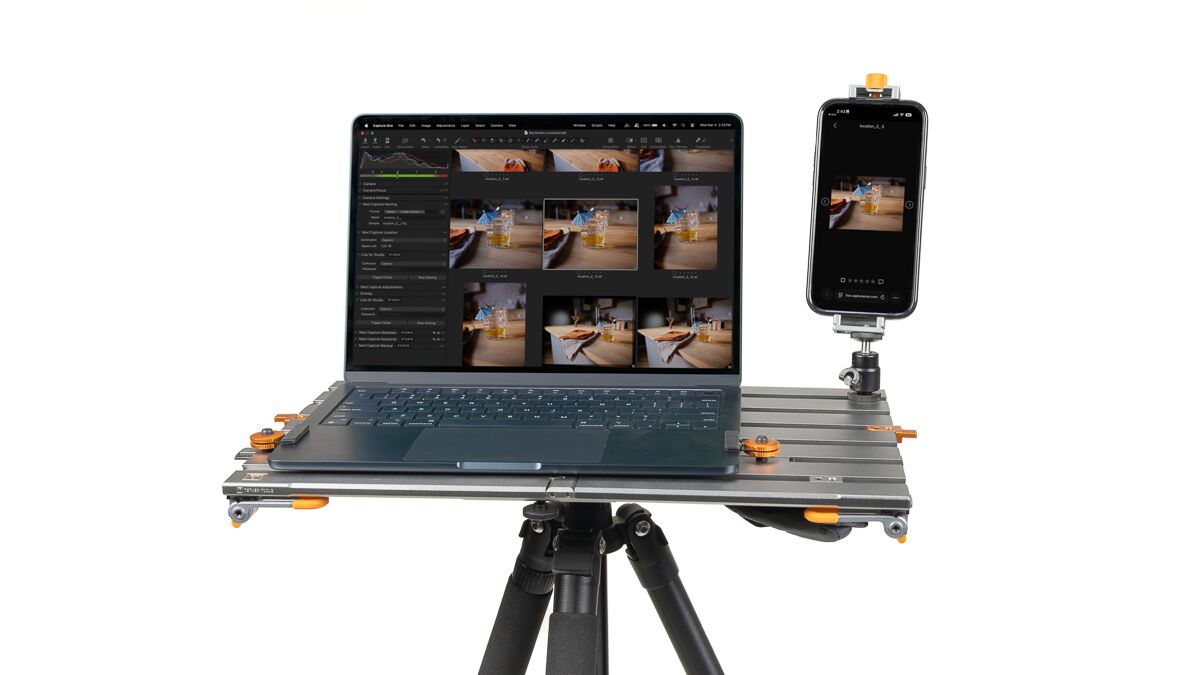 Laptop on a metal portable rig with a mounted smartphone, set on a tripod for mobile editing.