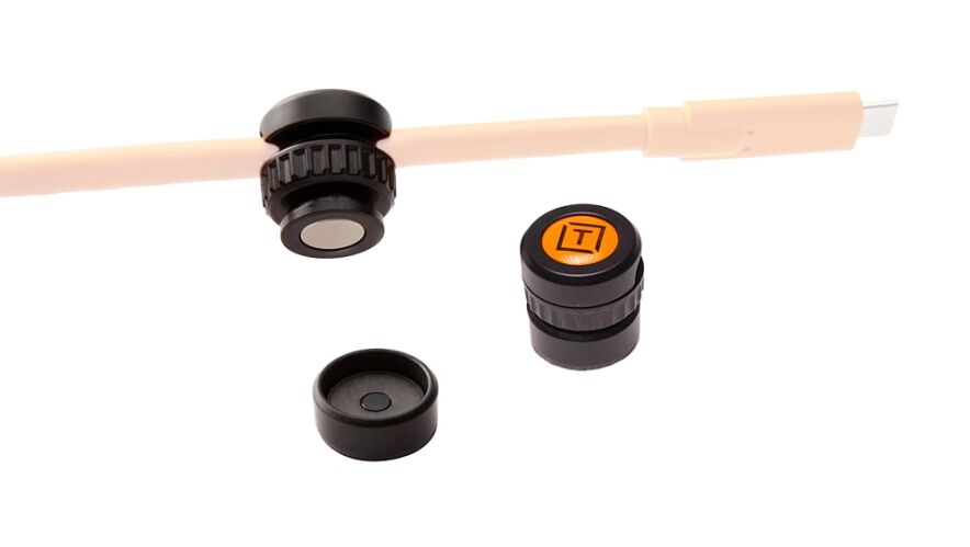 Set of three black caps with one orange top cap bearing a logo, arranged near a beige rod on a white background