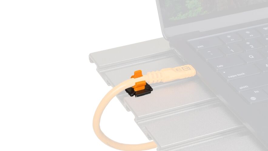 Close-up of an orange Ethernet-like cable plugged into a slim, silver docking module beside a laptop keyboard.