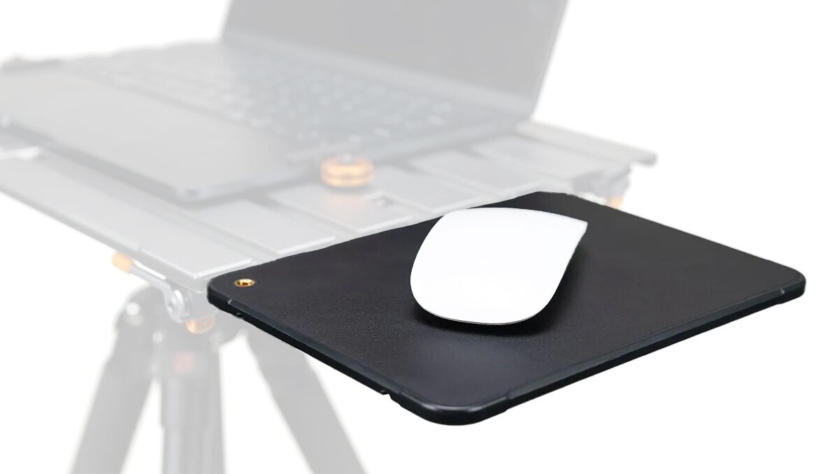 White wireless mouse resting on a black mousepad with a laptop blurred in the background, suggesting a desk setup for computing.