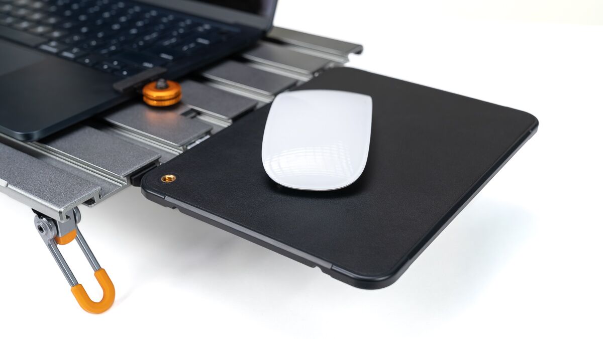 White wireless mouse resting on a black external hard drive dock attached to a laptop, with an orange latch visible nearby.