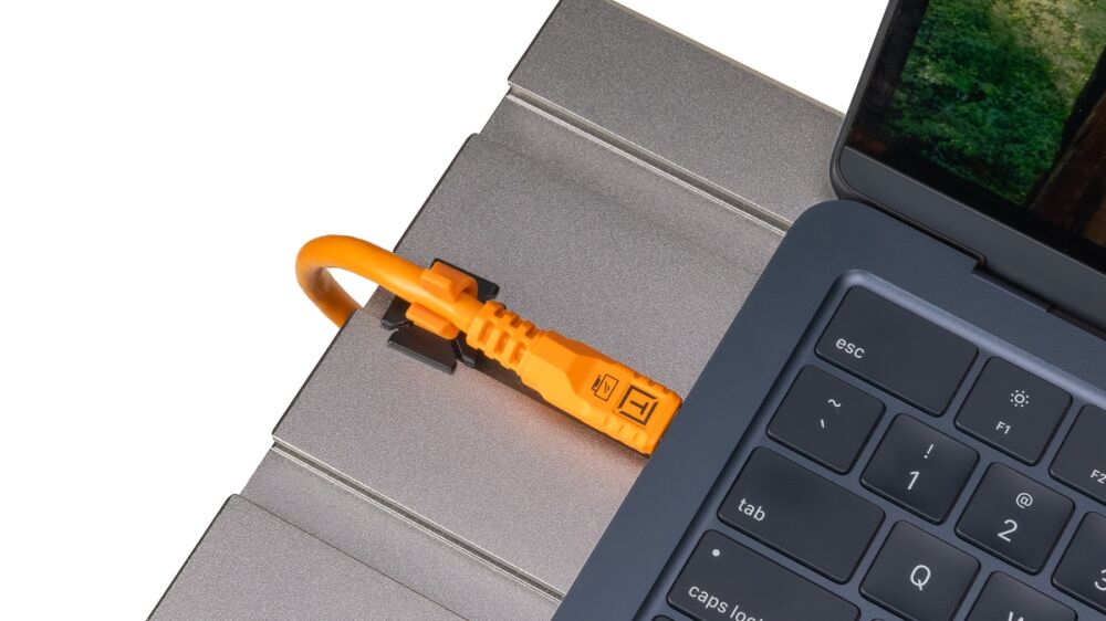Orange USB-C security lock plugged into a laptop port on a gray laptop edge