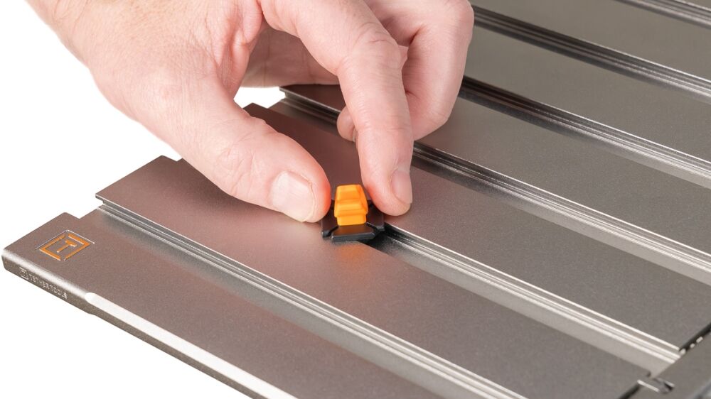 Close-up of a hand inserting an orange adjustment knob into a grooved metal surface.