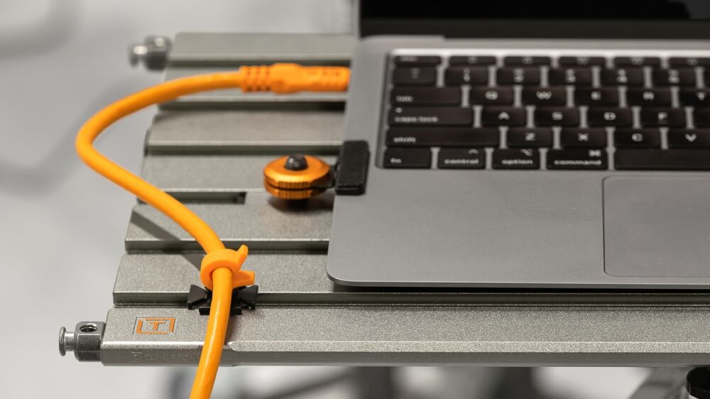 Laptop on a metal rack with an orange network cable plugged into it, illustrating a data connection setup on equipment.