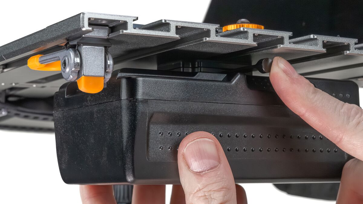 Close-up of a person adjusting a modular camera slider with orange locking levers on a black base.