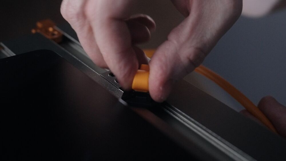 Close-up of a hand inserting a yellow plug into a panel while an orange cable runs nearby, suggesting a cable connection.