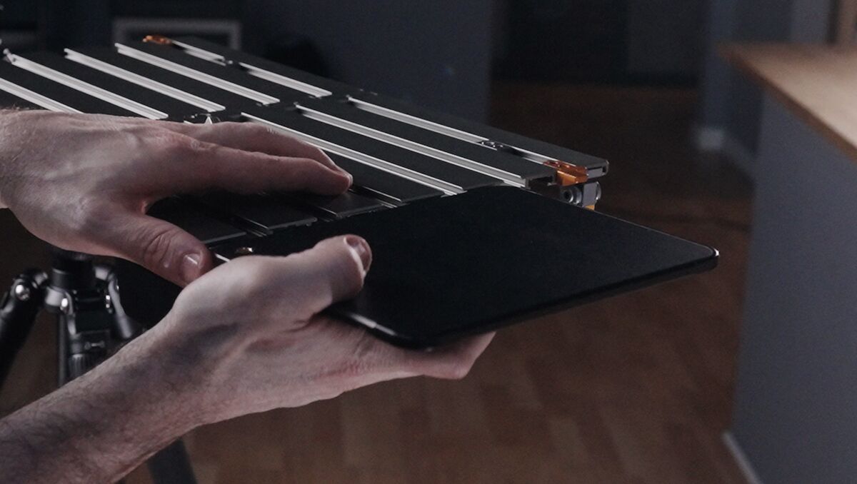 Person holding a tablet next to a metal camera slider/rig in a studio setting.