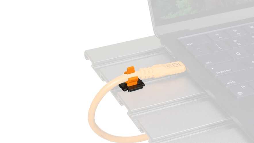 Close-up of an orange Ethernet-like cable plugged into a slim, silver docking module beside a laptop keyboard.