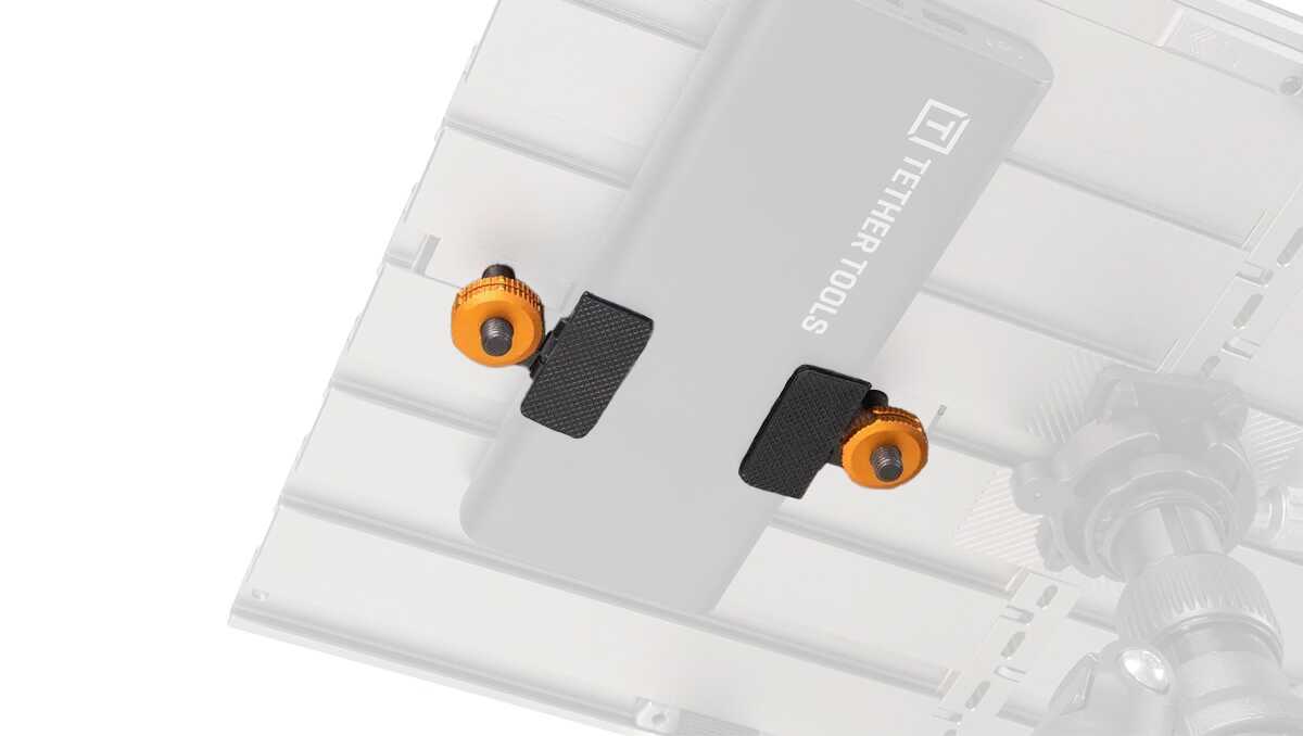 Close-up of a gray camera mounting plate with two black clamp pads and orange thumbscrews on a metal rig.