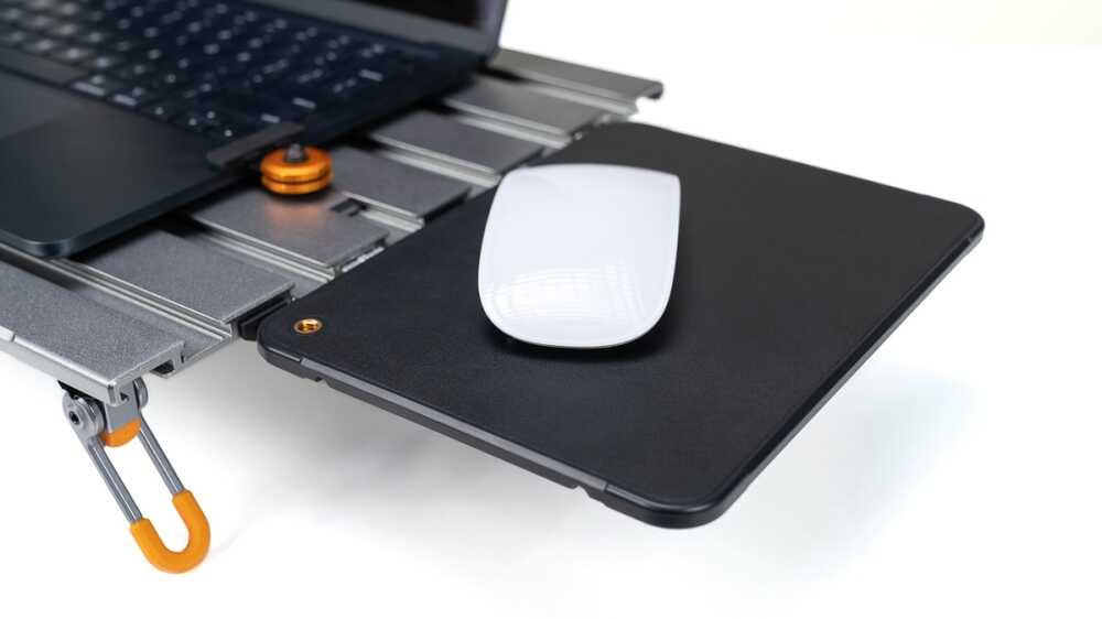 White wireless mouse resting on a black external hard drive dock attached to a laptop, with an orange latch visible nearby.