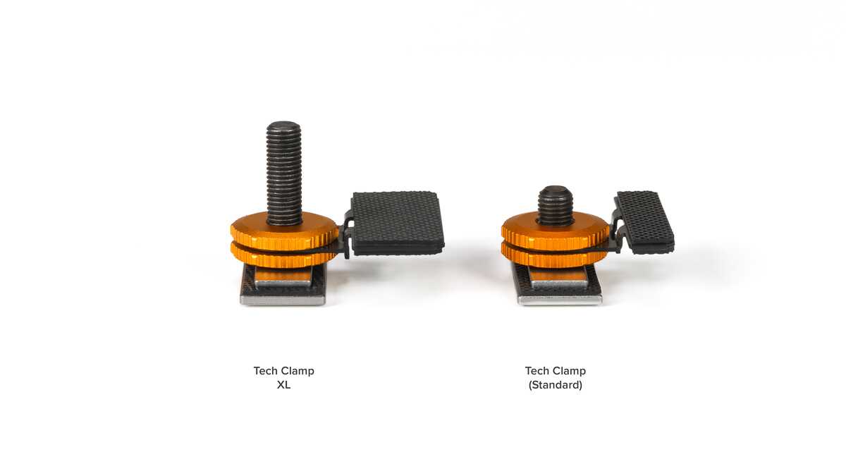 Two orange Tech Clamps on a white background: left is XL with a tall bolt and black pedal, right is Standard with a shorter bolt and pedal.