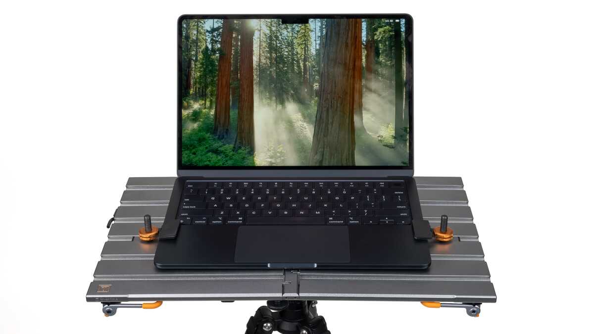 Slim black laptop placed on a metallic modular platform mounted on a tripod, forest scene on screen.