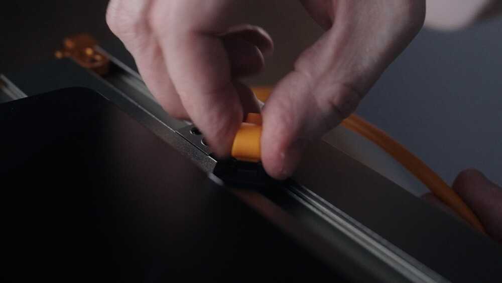 Close-up of a hand inserting a yellow plug into a panel while an orange cable runs nearby, suggesting a cable connection.
