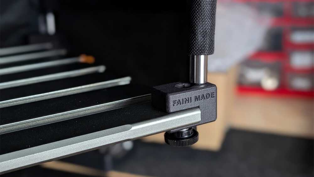 Close-up of a 3D printer bed clamp with a black textured knob securing the bed rail.