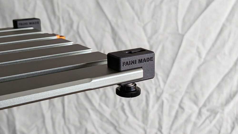 Close-up of a silver T-slot rail with a black clamp block labeled 'FANI MADE' secured by a round knurled adjustment knob beneath the block.