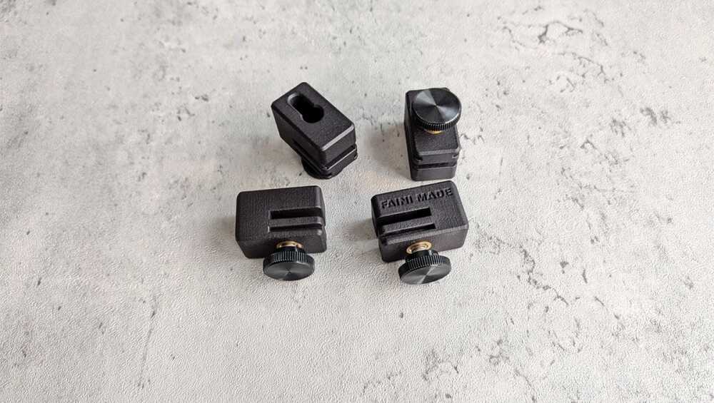 Four small black clamping blocks with adjustment knobs spread on a gray textured surface