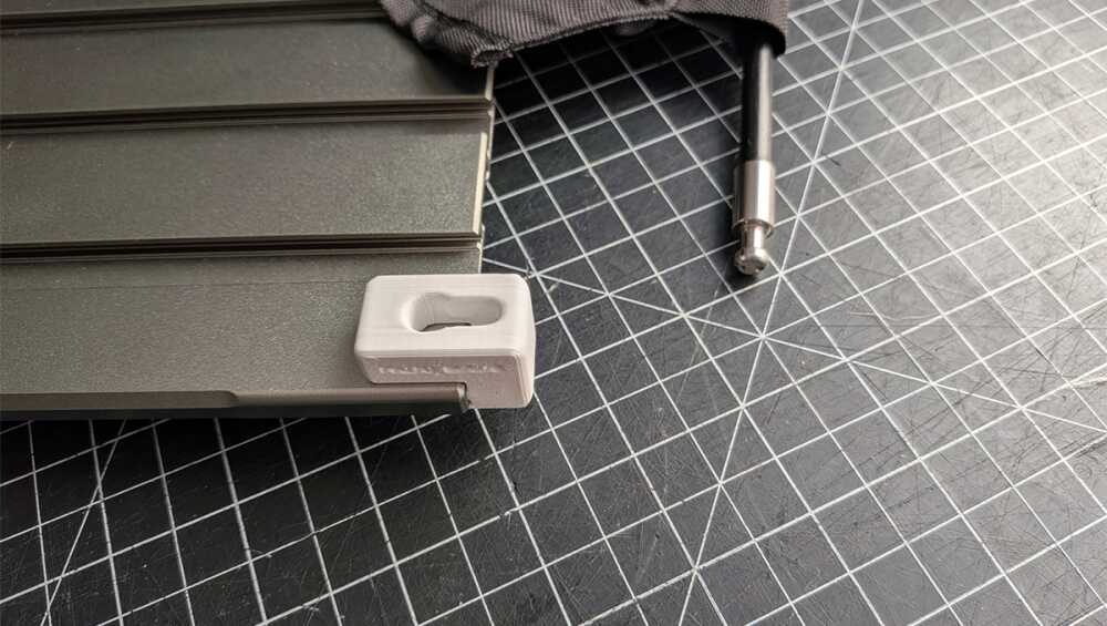 Close-up of a gray metal toolbox accessory with a small white plastic end cap on a grid-cutting mat.