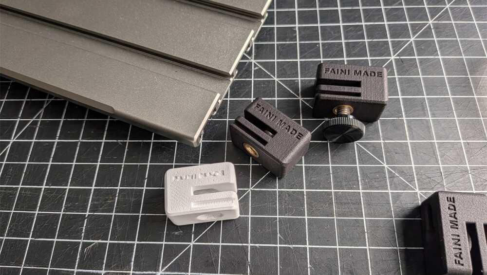 Assorted small plastic clamps on a dark grid cutting mat, with a stack of gray metal pieces to the left.