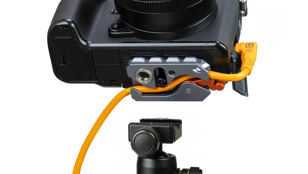 Close-up of a DSLR camera attached to a gray battery grip with an orange power cable plugged into the bottom port, on a tripod head