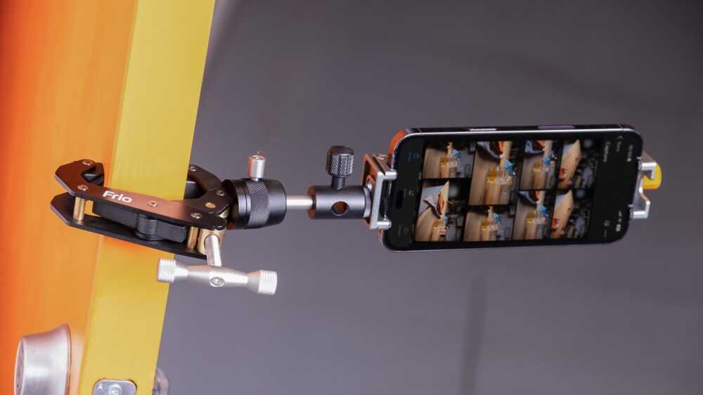 Smartphone mounted on a metal rig photographing a yellow-orange wooden beam; the screen shows a grid of captured shots.