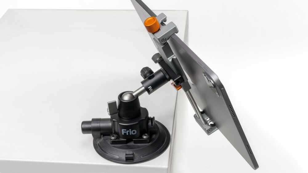 Flat-screen monitor mounted on an adjustable arm clamp attached to a white surface with an orange adjustment knob visible.