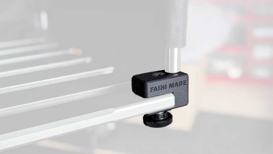 Close-up of a black clamping accessory attached to a silver aluminum rail, securing a workpiece in a workshop setup