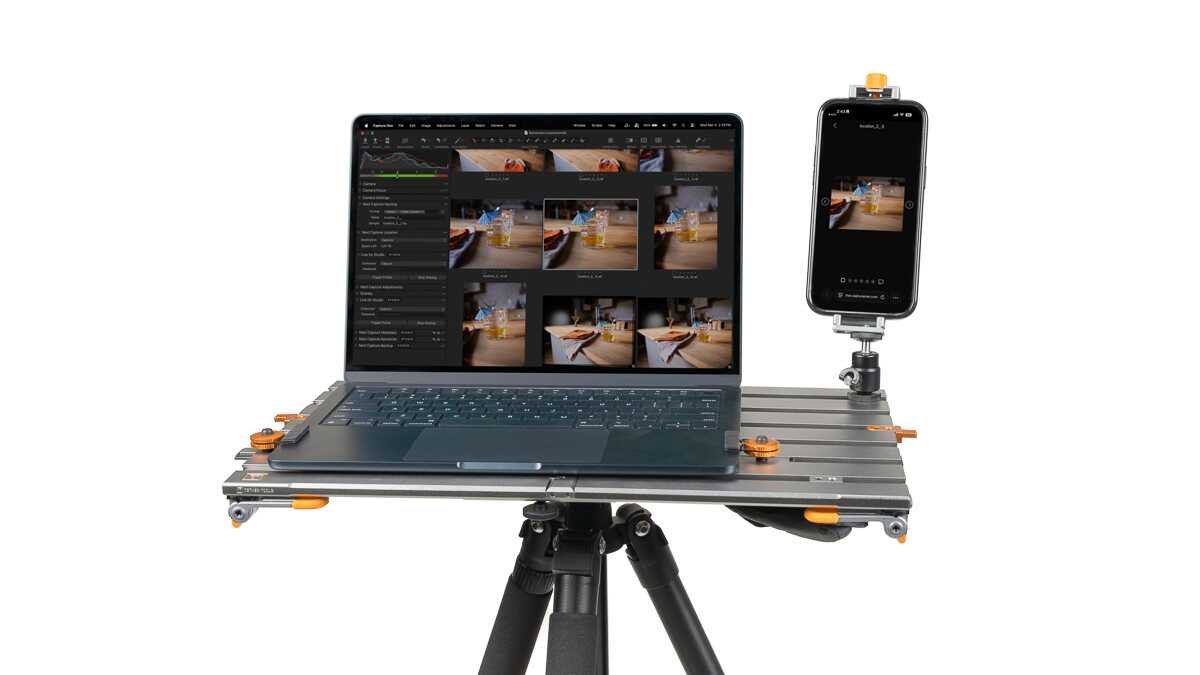 Laptop on a metal portable rig with a mounted smartphone, set on a tripod for mobile editing.