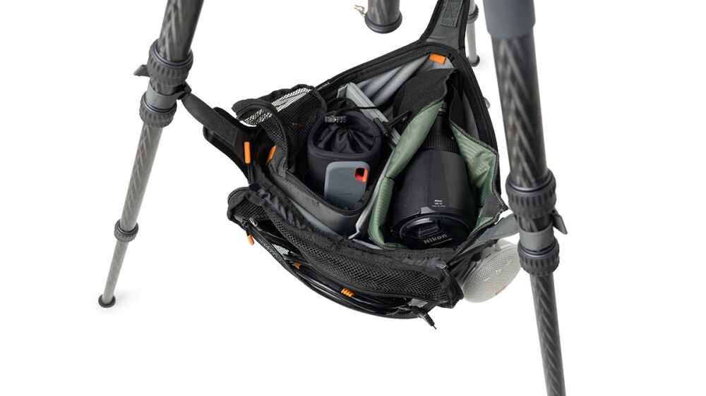Open camera bag attached to a tripod, revealing a camera body, lens, and accessories inside.