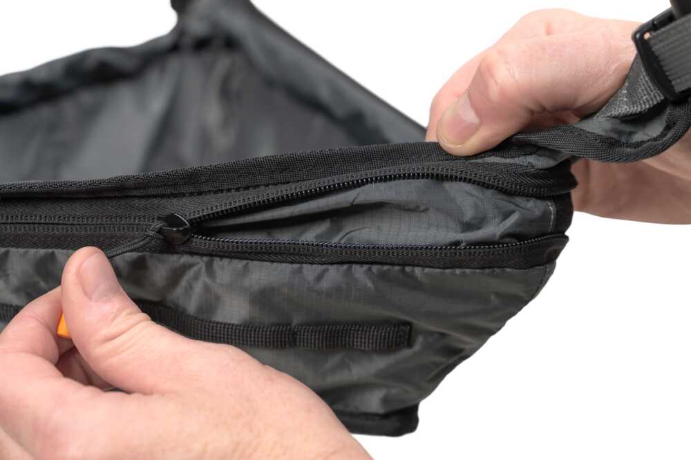 Close-up of hands unzipping a gray nylon bag or pouch, showing the zipper and fabric edge.