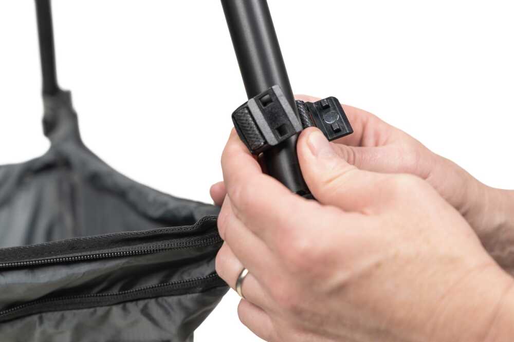 Hands tighten a plastic quick-release clamp on a black telescoping pole near a zipped bag.