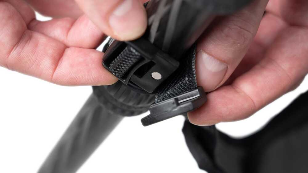 Close-up of hands fastening a black plastic buckle on a textured strap (likely a bag or tripod strap).