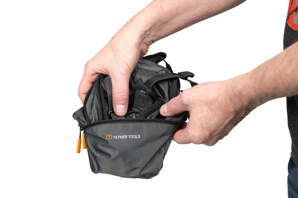 Hands unzipping a small gray pouch labeled Tether Tools with orange zipper pulls