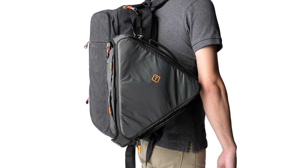 Person wearing a dark gray backpack with a diagonal front sleeve and orange zipper pulls