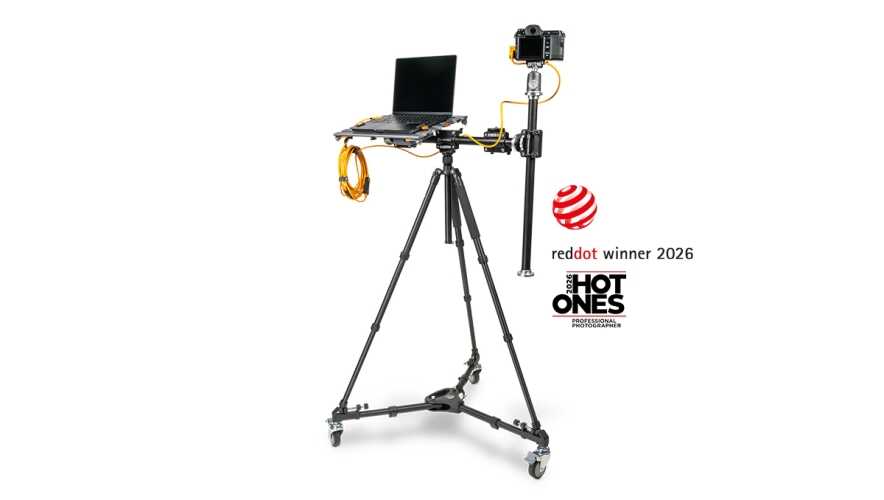 Camera rig on a wheeled tripod with a laptop and camera mounted on a vertical arm; orange cables extend from the setup, with red dot winner 2026 and HOT ONES logos nearby.