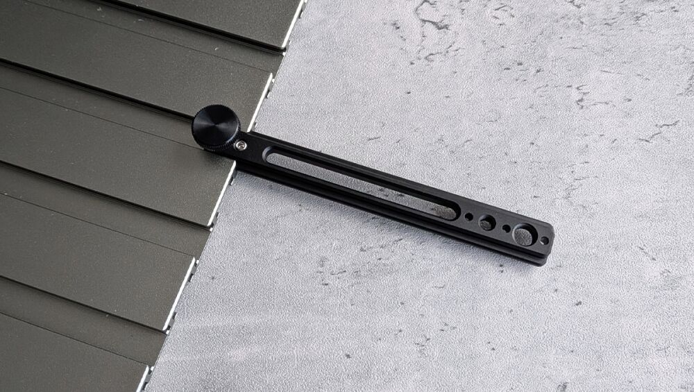 Black adjustable mounting rail with a circular knurled knob resting on dark rooftop panels; used to secure components to a surface.