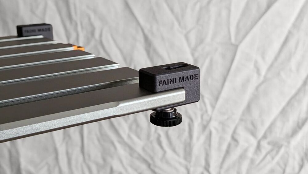 Close-up of a silver T-slot rail with a black clamp block labeled 'FANI MADE' secured by a round knurled adjustment knob beneath the block.