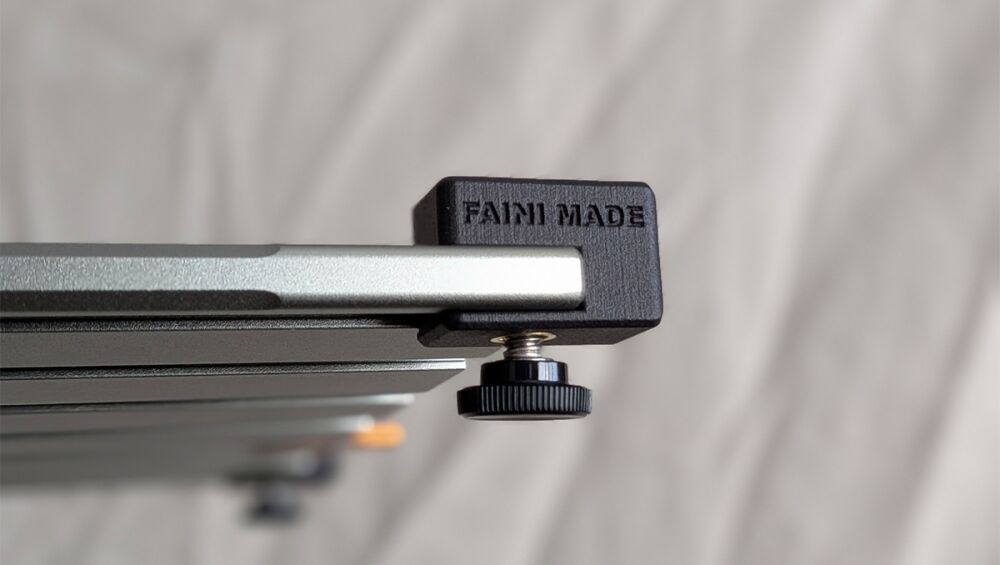 Close-up of a metal camera slider rail with a black end block and a knurled adjustment knob.
