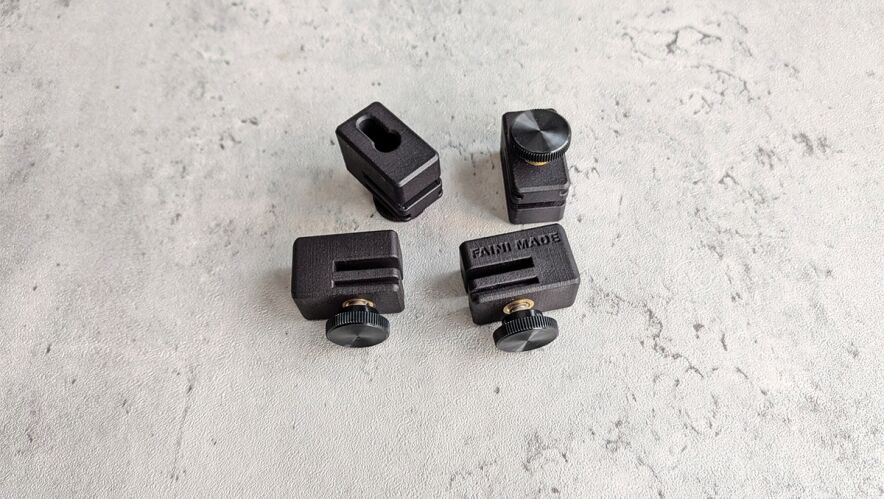Four small black clamping blocks with adjustment knobs spread on a gray textured surface