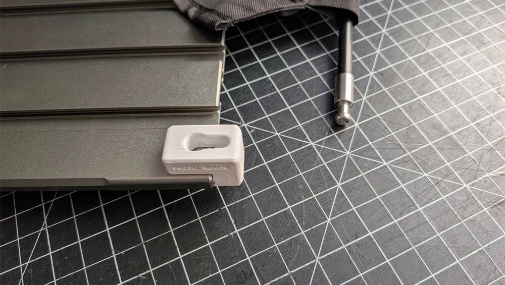 Close-up of a gray metal toolbox accessory with a small white plastic end cap on a grid-cutting mat.