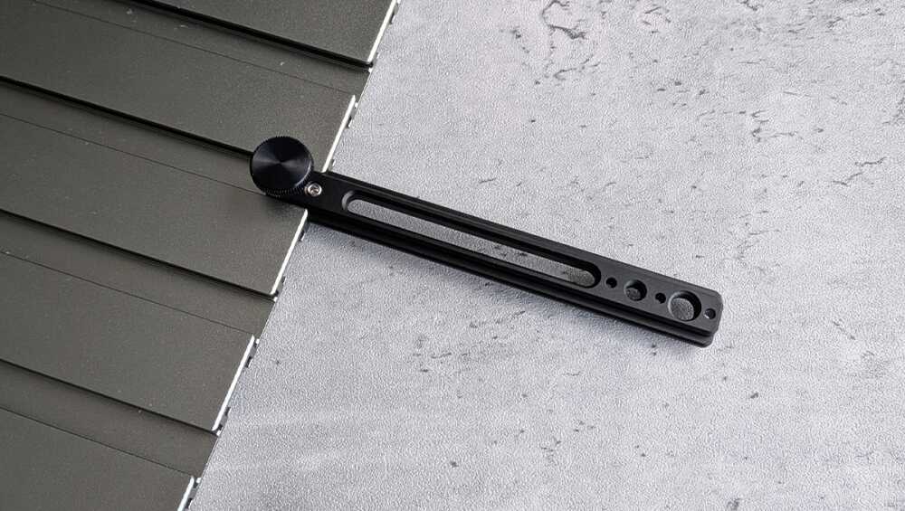 Black adjustable mounting rail with a circular knurled knob resting on dark rooftop panels; used to secure components to a surface.