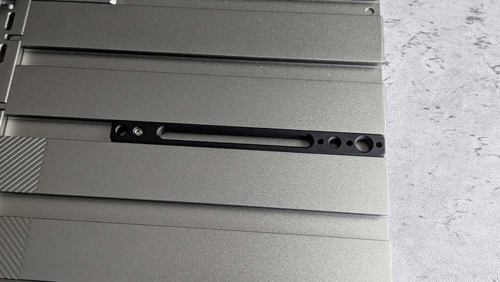 Close-up of a gray metal panel featuring a long black carriage/slot with small circular holes along the edge, likely a mounting or retention area on hardware.