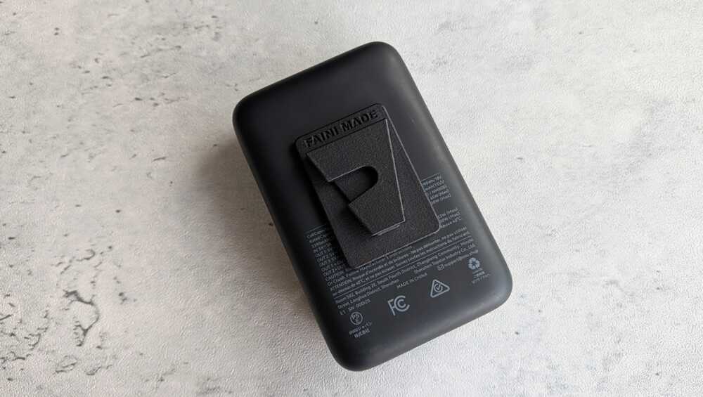 Back of a black rectangular charger with a fold-out clip on a light gray textured surface.