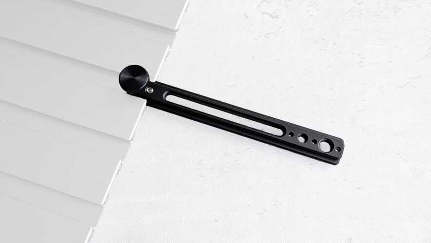 Close-up of a black metal blind tilt rod with a round knob resting against white window blinds on a light surface, showing the adjustment hardware.