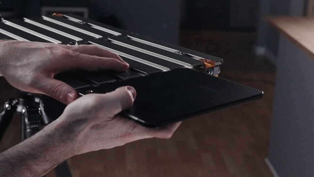 Person holding a tablet next to a metal camera slider/rig in a studio setting.