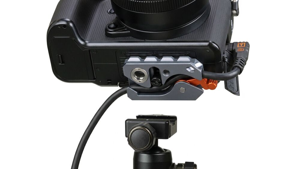 Close-up of a camera's bottom with a modular mounting rig and orange quick-release lever, connected by a cable to an accessory.