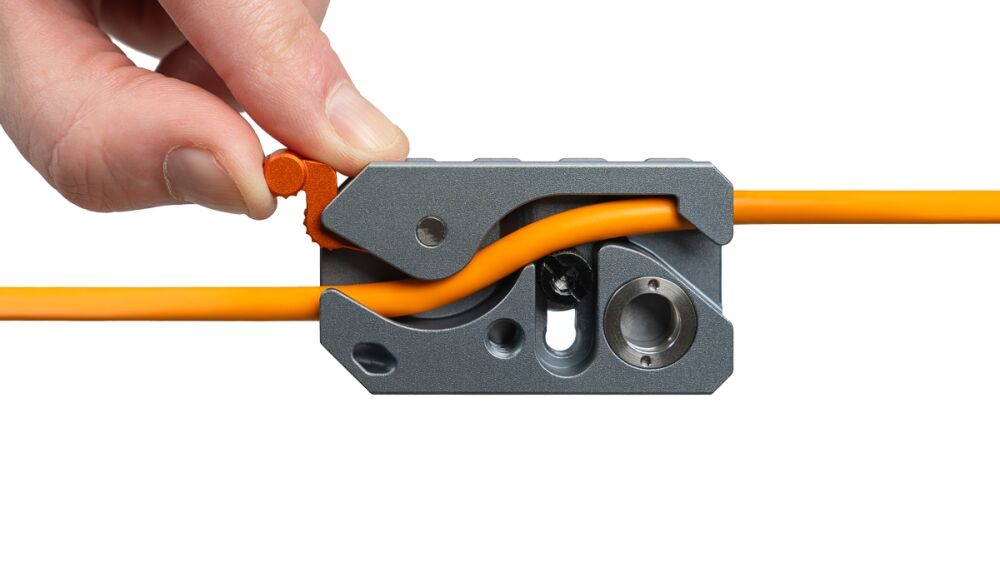 Hand using a crimp/wire stripper tool on an orange electrical wire, close up