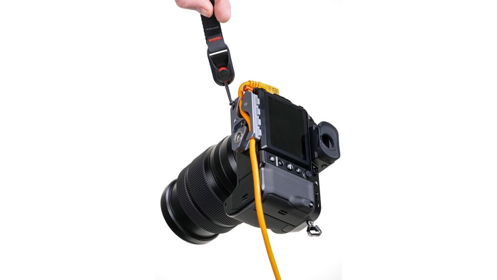 DSLR camera with attached screen and orange cable, held by hand with strap.