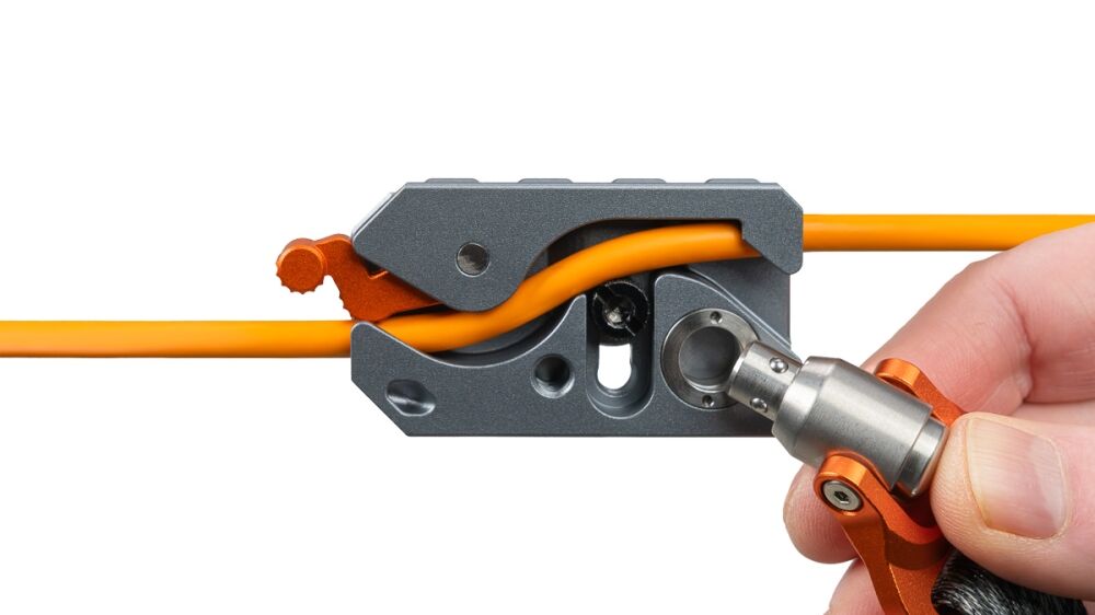 Close-up of a hand operating a precision wire stripper/crimping tool on an orange electrical wire to strip insulation or crimp a connector.