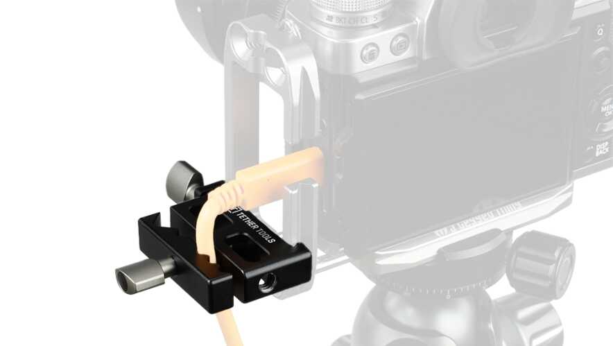 Close-up of a black camera cable clamp securing an orange cable to a camera rig on a tripod head.